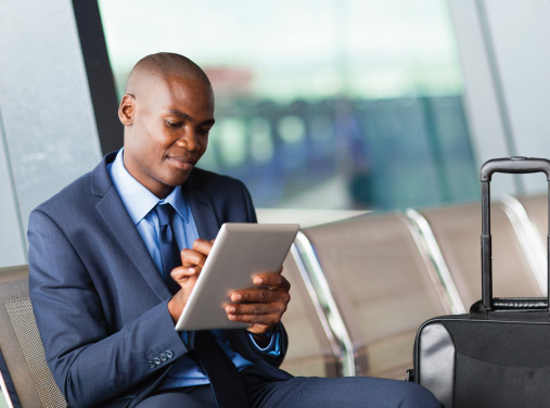 Business Man At The Airport Using His Tablet Device To Sign-in to the CAP Travel Risk Portal