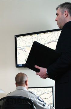 Travel Manager Working With Security Specialists To Monitor Travelers on Maps Displayed on Digital Screens