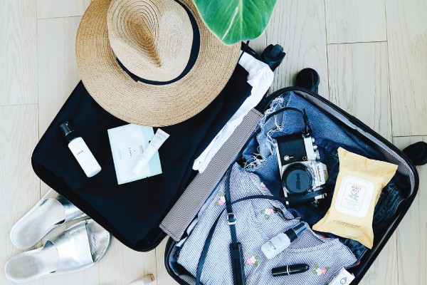 Messy open suitcase filled with summer attire and travel accessories